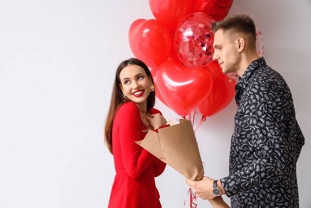 Young man greeting his girlfriend for Valentine's Day on light background - 写真・画像