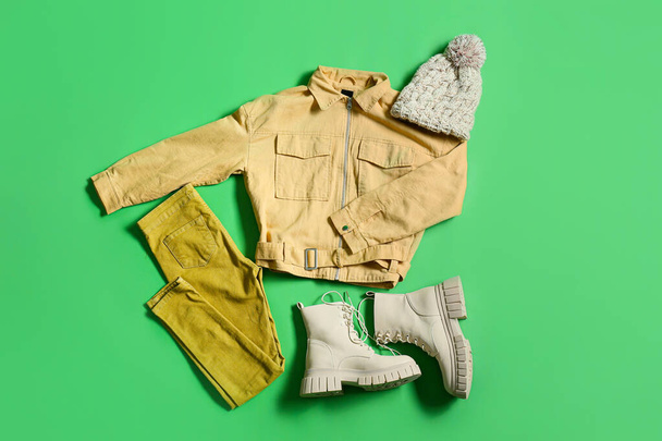 Female jacket, pants, knitted hat and shoes on green background - Fotó, kép