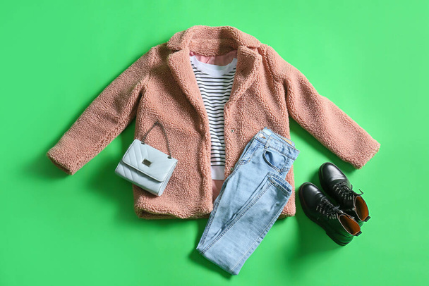 Kışlık ceket, süveter, kot pantolon, ayakkabı ve çanta yeşil arka planda. - Fotoğraf, Görsel