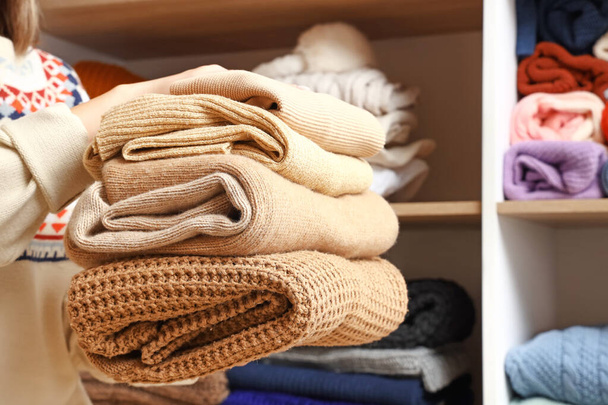 Жінка зі стопкою в'язаних светрів в гардеробі, крупним планом
 - Фото, зображення