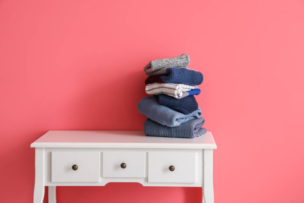Στοίβα από ζεστά πλεκτά πουλόβερ στο τραπέζι κοντά σε ροζ τοίχο - Φωτογραφία, εικόνα