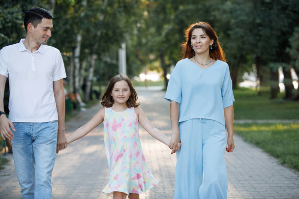 娘のいる家族カップルが夏の公園の道を歩いています。幸せな子供時代。親としてのケア。選択的焦点、ぼやけた背景. - 写真・画像