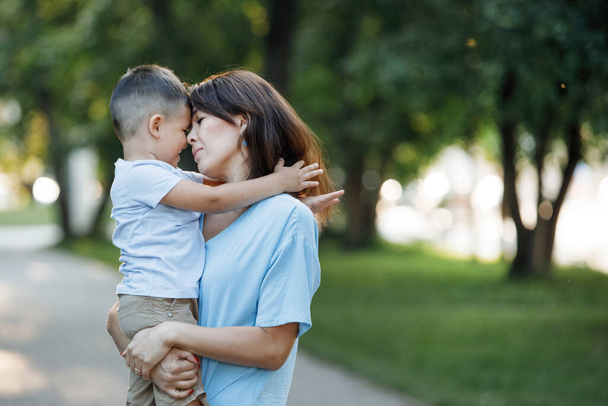 Mamá abraza y besa a su hijo en el parque de verano. Enfoque selectivo, fondo borroso. Feliz infancia. Cuidado de los padres. - Foto, Imagen