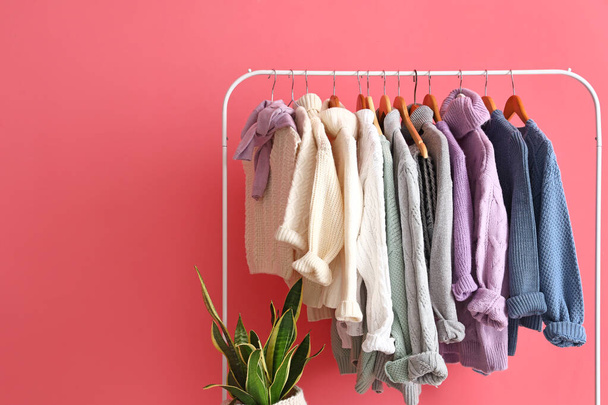 Stojak ze stylowymi, ciepłymi swetrami przy różowej ścianie - Zdjęcie, obraz