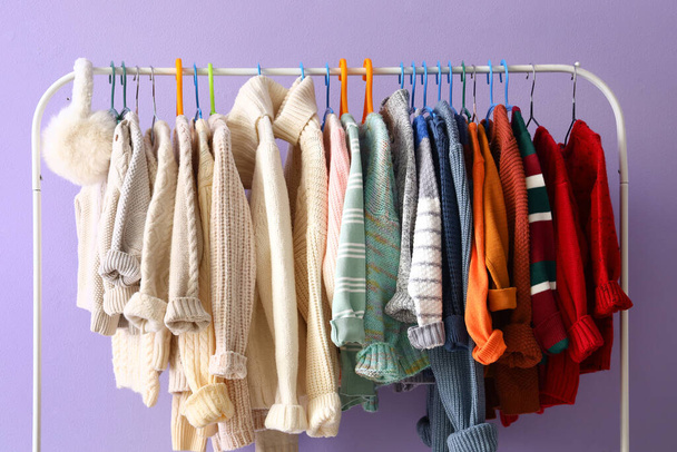 Стойка с детскими свитерами и наушниками рядом со стеной сирени - Фото, изображение