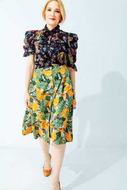 Pretty blonde with short hair in a yellow skirt with a green floral print stands on a white backgroun - Foto, Bild