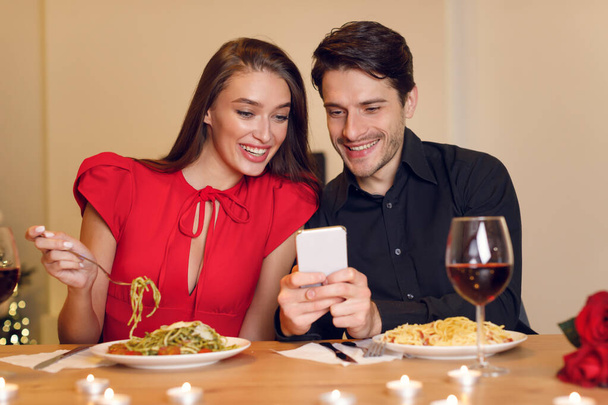 Homme et femme souriants utilisant le téléphone portable pendant le dîner - Photo, image