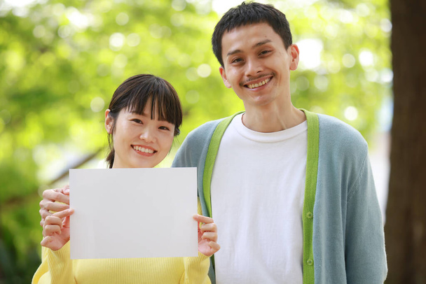 feliz asiático pareja holding en blanco papel en el parque - Foto, imagen