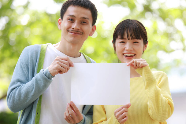 Happy asian couple holding blank paper in the park - Zdjęcie, obraz