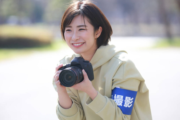 Hymyilevällä naisvalokuvaajalla on kädessään käsinauha, jossa lukee "ammunta" japaniksi.. - Valokuva, kuva