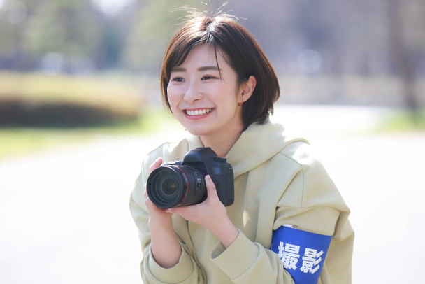 Egy mosolygó női fotósnak van egy karszalag a karján, amin az áll, hogy "lövés" japánul.. - Fotó, kép