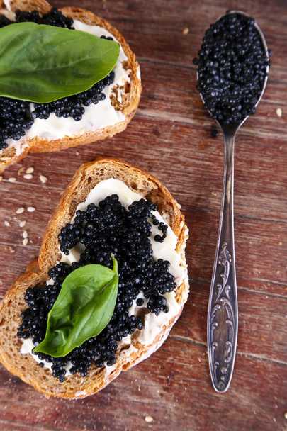 Slices of bread with butter and black caviar on wooden background - Фото, зображення