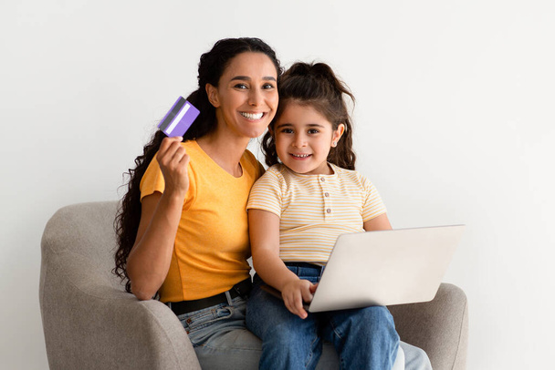 Compras en línea. Madre y lindo niño femenino con computadora portátil y tarjeta de crédito - Foto, imagen