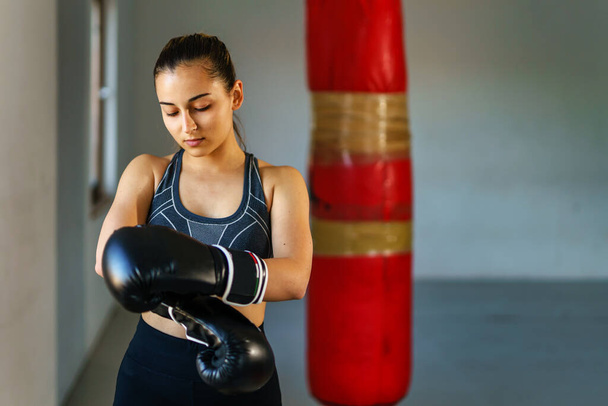 Front view portrait of young caucasian woman or teenage girl wearing boxing gloves - female boxer adjusting gloves waist up copy space - Photo, Image