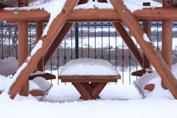 Snow on the table and benches of the gazebo against the background of a forged fence and meadows - Foto, immagini