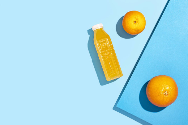 Детоксикационный сок в пластиковой бутылке, апельсины на синем фоне. Вид сверху, плоский - Фото, изображение