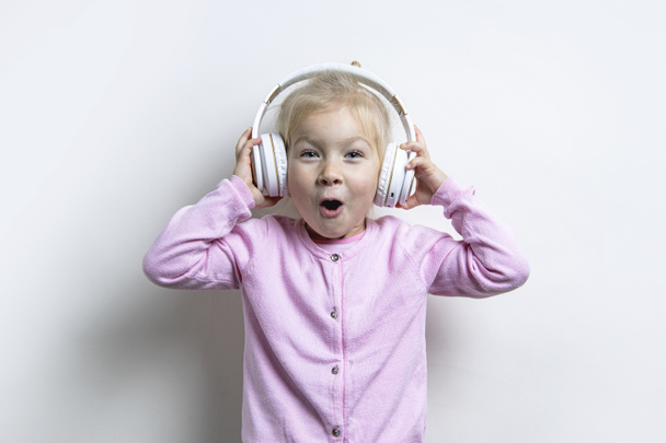 Surprised child girl in headphones looks up on a light background - 写真・画像