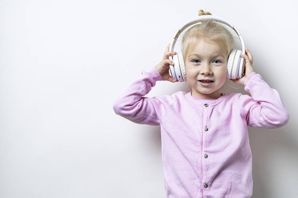 Hymyilevä lapsi tyttö valkoisissa kuulokkeissa kevyellä taustalla  - Valokuva, kuva