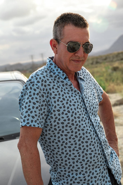 ein 60-jähriger Mann, der sich selbst pflegt, gesund und attraktiv ist und im Auto mit seinem blauen Hemd posiert - Foto, Bild