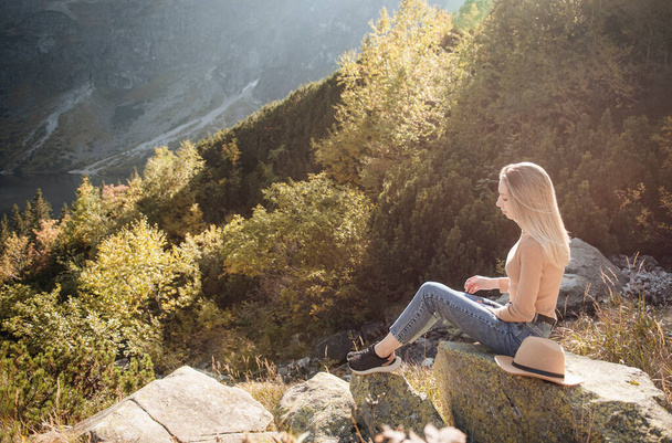 Mladá žena turista sedí na vrcholu hory a krásné hory. Krajina se sportovními dívkami, zelený les, kopce, nebe, jezero. Cestování a cestovní ruch. - Fotografie, Obrázek