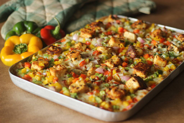 Paneer, mozzarella peyniri, kırmızı yeşil kapsiyomlar ve soğanlarla dolu ev yapımı pizza. Dikdörtgen bir tepside pişirilmiş. - Fotoğraf, Görsel
