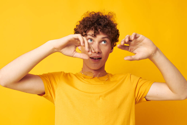 portrait of a young curly man yellow t-shirt glasses fashion hand gestures monochrome shot - Foto, imagen