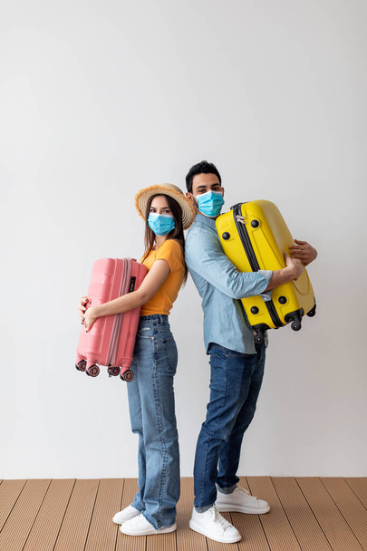 Touristen in Gesichtsmasken umarmen ihre Koffer und stehen über einer Lichtwand. Geimpfte Ehepartner urlaubsreif - Foto, Bild