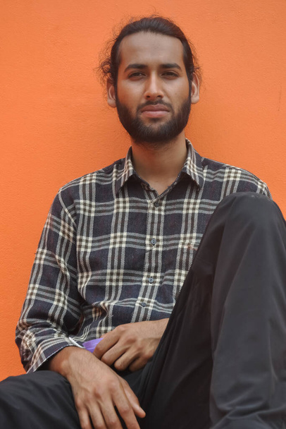 Front view of a attractive bearded young man looking at camera, sitting against orange wall background with copy space  - Photo, Image