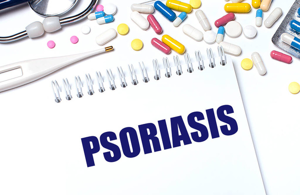 On a light background, multi-colored pills, a stethoscope, an electronic thermometer and a notebook with the text PSORIASIS. Medical concept. - Foto, immagini