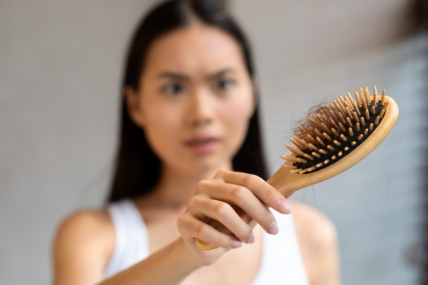 Worried millennial asian woman holding hairbrush, closeup - 写真・画像