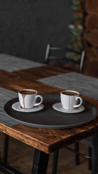 Dwie filiżanki kawy stoją na tacy w restauracji. ciemne kolory, wnętrze w stylu poddasza. brak ludzi - Zdjęcie, obraz
