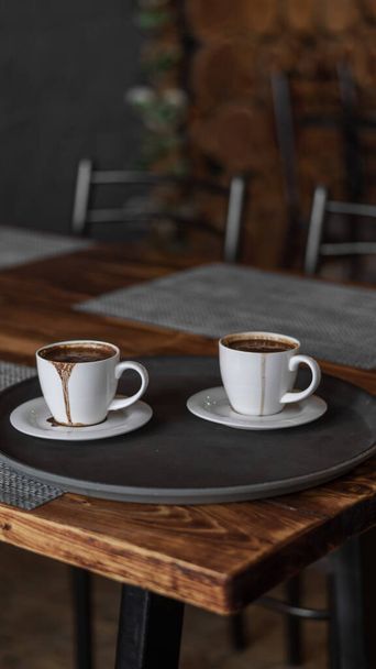 two mugs of coffee stands on a tray in a restaurant.  dark colors, loft style interior.  no people - Φωτογραφία, εικόνα