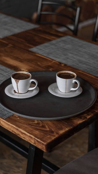 two mugs of coffee stands on a tray in a restaurant.  dark colors, loft style interior.  no people - Zdjęcie, obraz