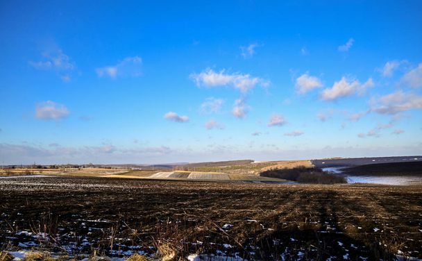 Hóval borított mezőgazdasági területek. Fekete föld a hó alatt.Kék ég. - Fotó, kép