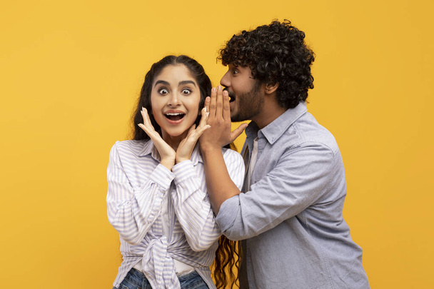 Shock, roddel, deel advies. jonge indiaanse man fluisteren naar dame op oor, verrast vrouw met open mond - Foto, afbeelding