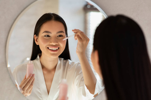 Zrcadlový odraz usměvavé ženy držící láhev s kosmetickým produktem - Fotografie, Obrázek