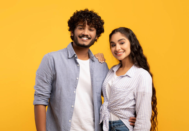 Romantic couple. Portrait of happy indian man and woman embracing and smiling at camera on yellow background - Fotografie, Obrázek