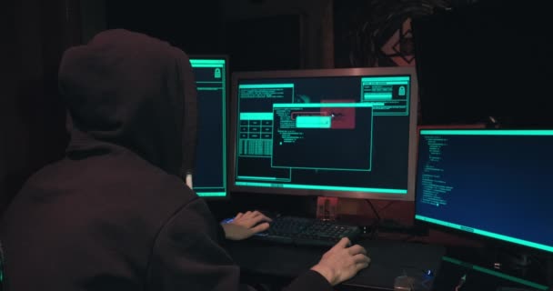 Hacker in un cappuccio siede di fronte a schermi di computer e database di hack - Filmati, video