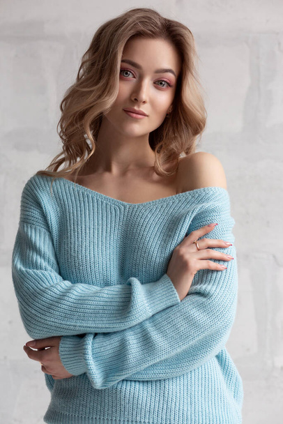 Sexy blonde girl in a blue knitted sweater on a white wall background - Fotografie, Obrázek