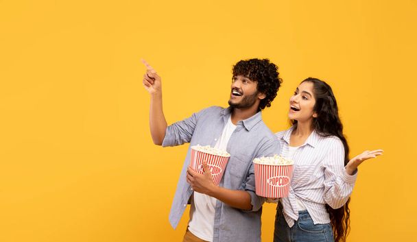 Happy indian couple eating popcorn, cheerful guy pointing at free space for advert or text, panorama - Foto, imagen
