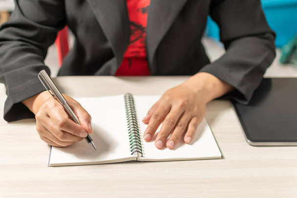 Close-up and selective focus of a woman's handwriting with a notebook placed on a wooden desktop. Concept businesswoman is keeping a record of planning marketing, investment, finance, banking, trading - Fotó, kép