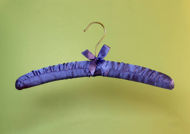 装飾的な弓と緑の背景に服のための紫色のリボンで飾られた1つの空のハンガー。スペースのコピー. - 写真・画像
