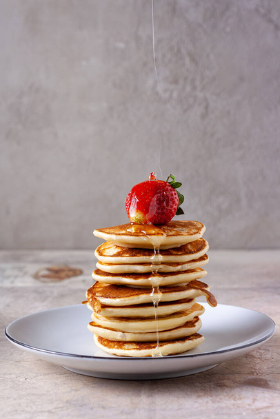 un sottile filo di miele si riversa sulle fragole su una pila di pancake - Foto, immagini