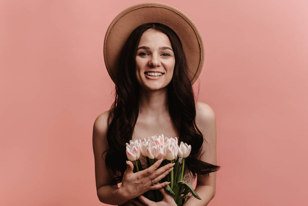 Retrato fotográfico de una joven sonriendo, sosteniendo un ramo de tulipanes, aislado sobre un fondo rosa pastel. - Foto, imagen