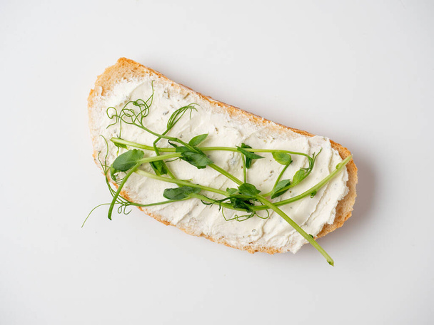 Gros plan d'une tranche de pain tartinée de fromage cottage et décorée de micro-verdure isolée sur fond blanc. Le concept d'une bonne nutrition. Snack sain, régime alimentaire. Vue de dessus, plan plat - Photo, image