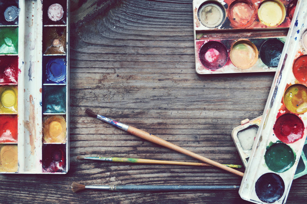 Colorful paints and brushes arranged as a frame on wooden table - Photo, Image