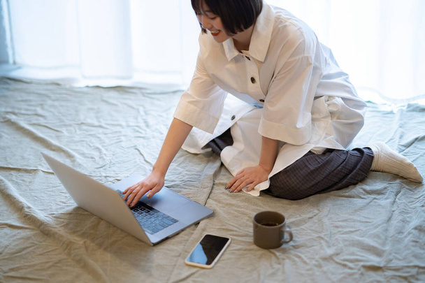 Женщина смотрит на ноутбук в непринужденной атмосфере в своей комнате - Фото, изображение