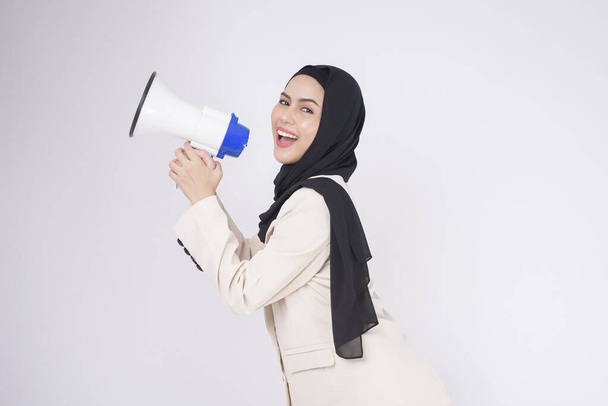 portrait of young beautiful muslim woman in suit using megaphone to announce over isolated white background studio - Zdjęcie, obraz