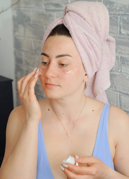 Young plus size woman applies clay to her face. Skin care at home. Beauty treatment. - Zdjęcie, obraz