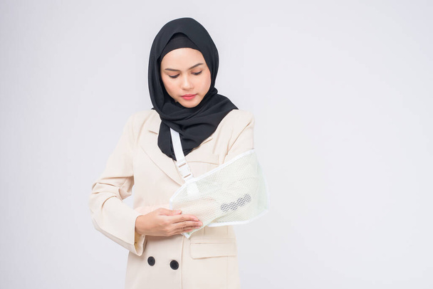 Portrait of young muslim woman with an injured arm in a sling over blue background in studio. - Foto, Imagem